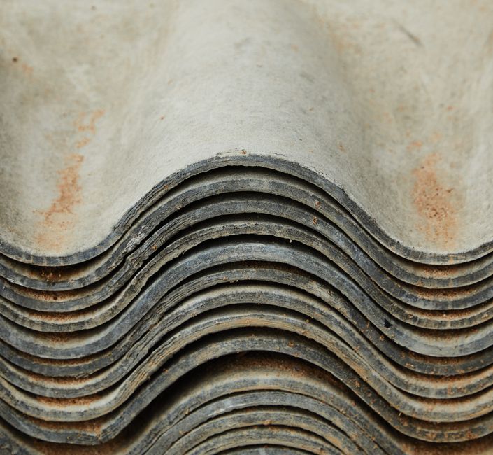 The image shows a close-up view of a grey, corrugated roof made of tiles, with a metallic vent pipe protruding from the surface. The vent pipe is cylindrical with a shiny, reflective cap on top, posit
