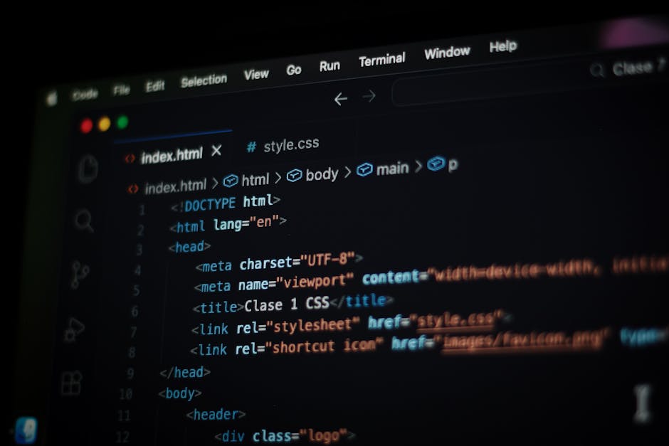 Close-up view of a MacBook Pro laptop on a desk displaying a dark-themed code editor with lines of JavaScript and HTML code related to application development, including functions, links, image tags, 